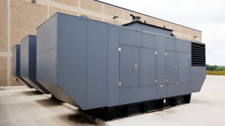 Three sizable, stationary standby generators painted in gray, positioned outdoors next to a building.