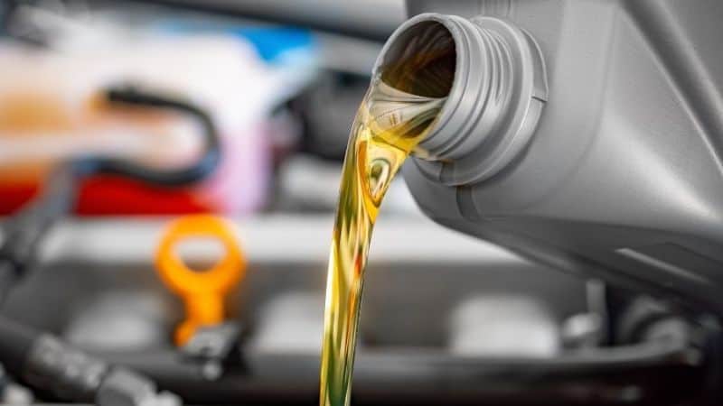 L'huile moteur est versée d'un récipient gris dans un moteur de voiture muni d'une jauge orange, rappelant de vérifier régulièrement l'huile du générateur.
