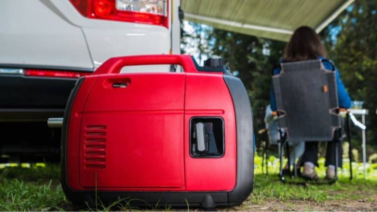 Red portable generator on grass by a parked vehicle; person sits on folding chair under awning in background.