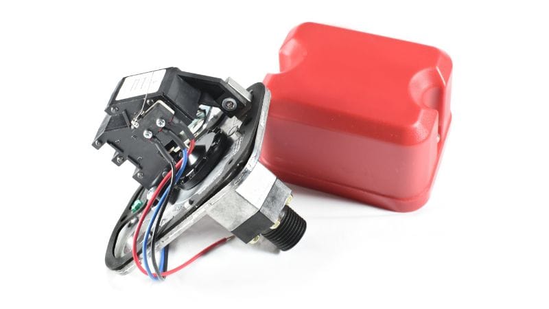 Mechanical pressure switch with exposed wiring, beside a red plastic cover, set against a white background.