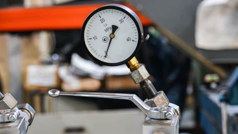 Pressure gauge reading just over 10 MPa on industrial equipment, with a metal lever beneath it.