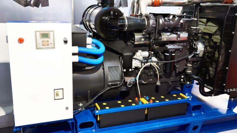 Générateur industriel avec panneau de commande, tuyaux de ventilation et batteries sur un cadre métallique bleu à l'intérieur.