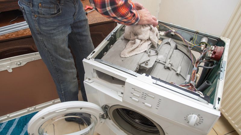 Clothes dryer repair technician fixing or cleaning the internal components of a front-loading washing machine.