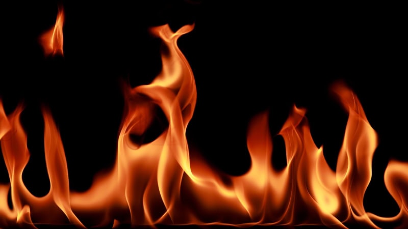 Brandende vlammen met intense oranje en gele tinten op een zwarte achtergrond, symboliseren warmte, energie en dynamische beweging.