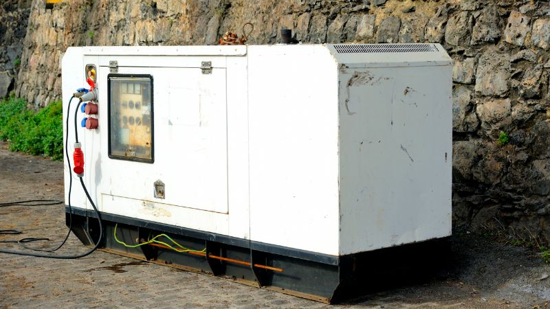 Generator de rezervă pentru alimentare fiabilă cu energie electrică în timpul întreruperilor de curent, instalat în exterior, lângă un zid de piatră, cu un design industrial durabil, esențial pentru locuințe și afaceri.
