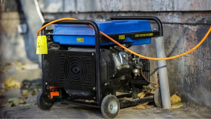 Heavy-duty water pump with orange hose for outdoor irrigation or construction use, mounted on a portable black frame with wheels, positioned against a brick wall.
